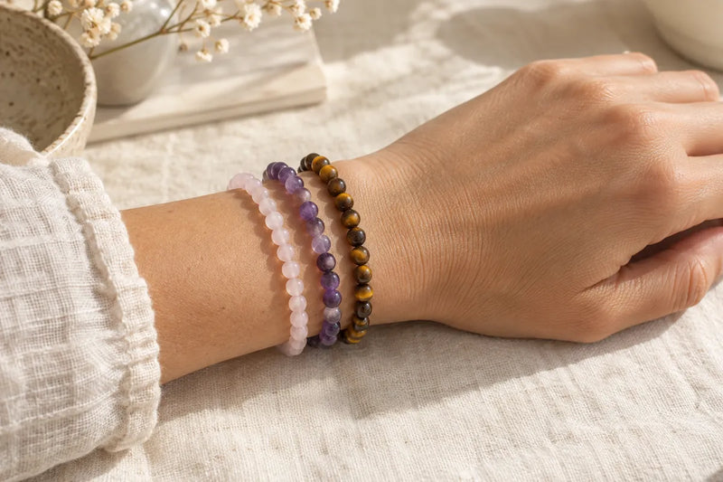Trois bracelets rose, violet et brun doré superposés sur un poignet.